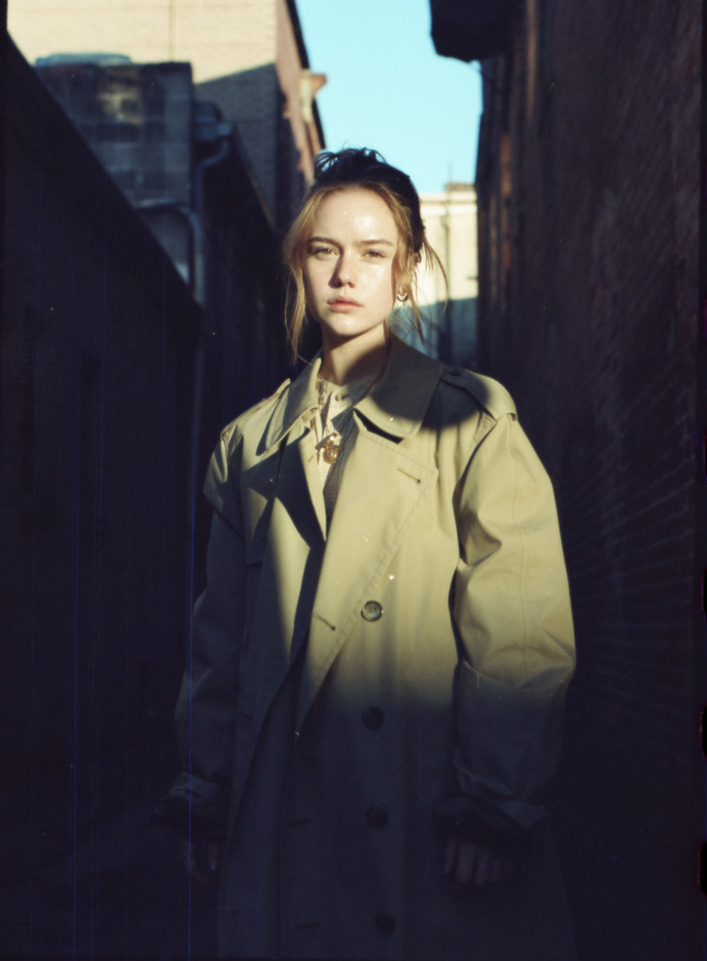 Film portrait in an oversized trench coat in a sunlit alley