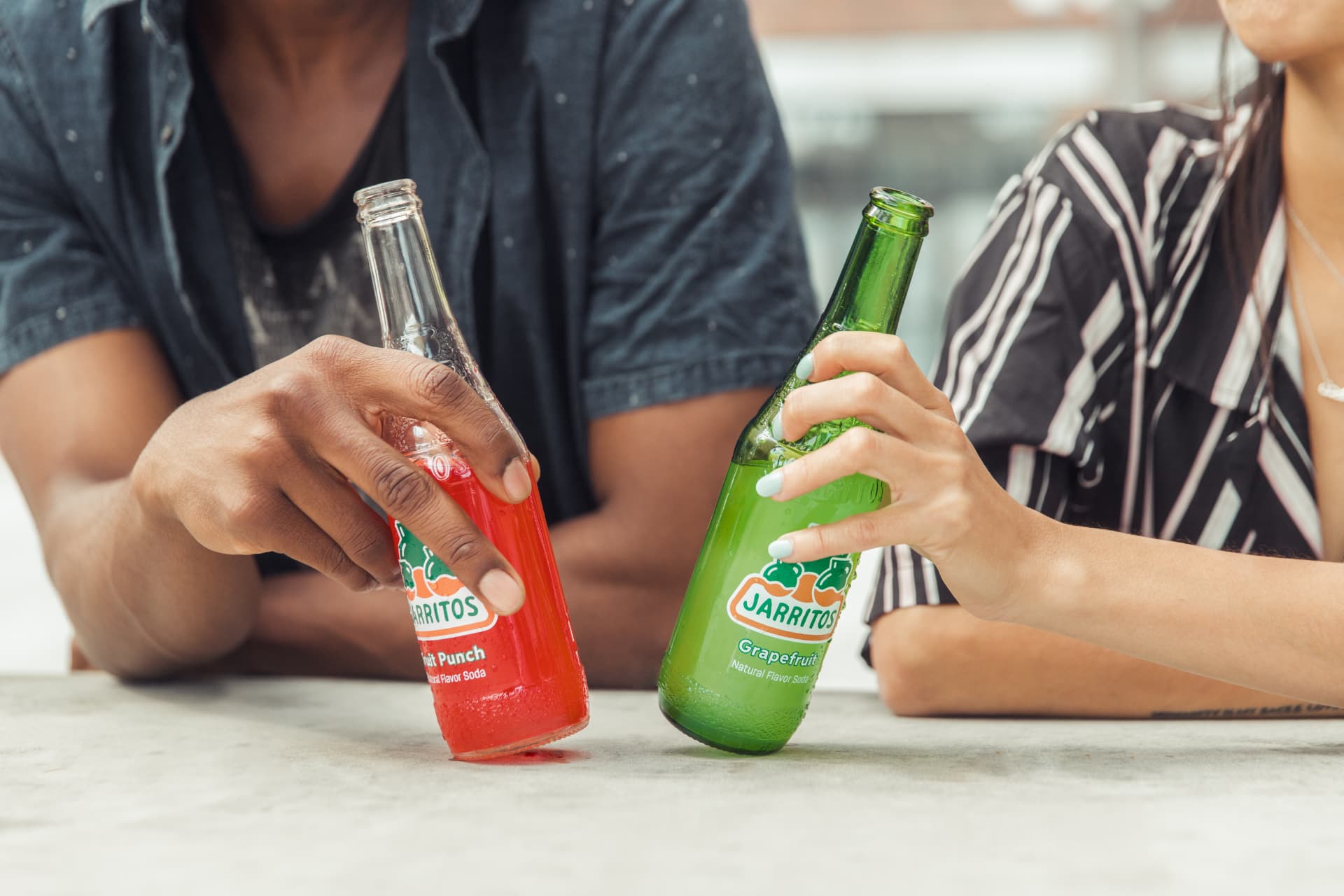Hands resting two Jarritos bottles on a concrete table