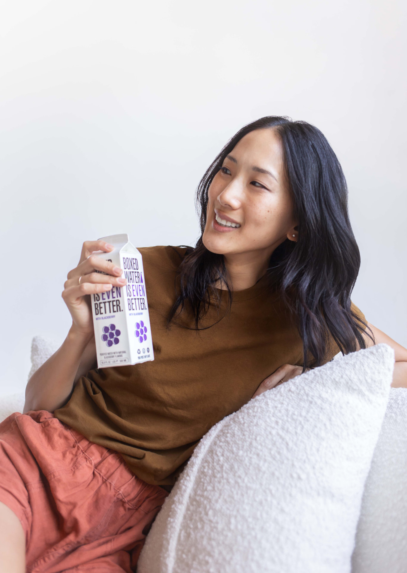 Woman in a brown tee on a sofa holding a blackberry Boxed Water carton