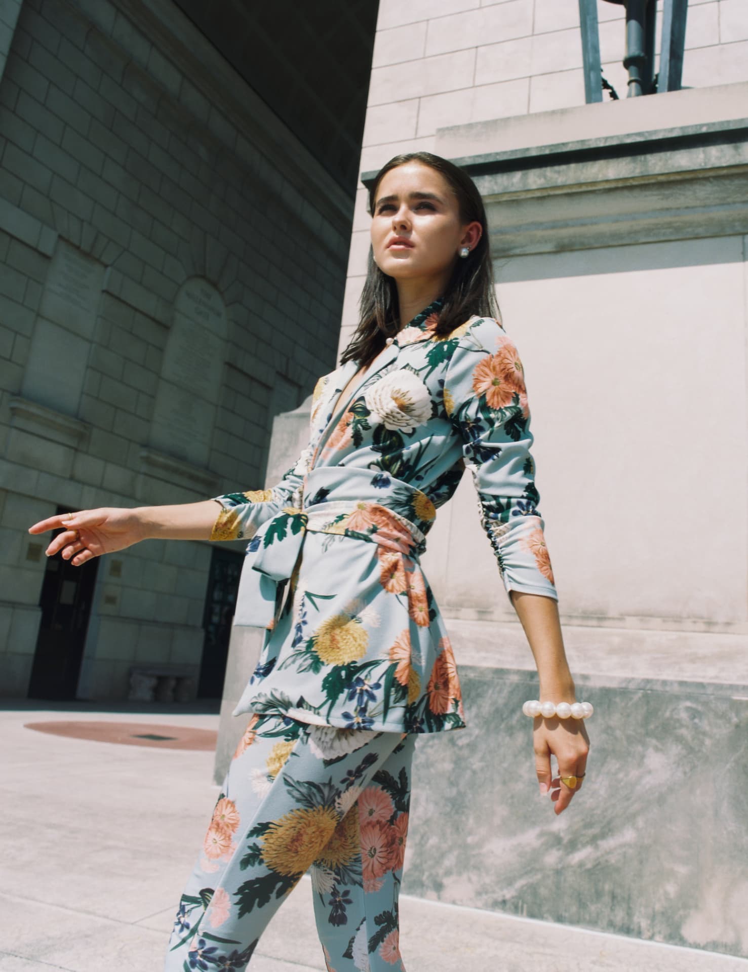 Portrait in a floral pastel suit walking past a stone building in hard sun