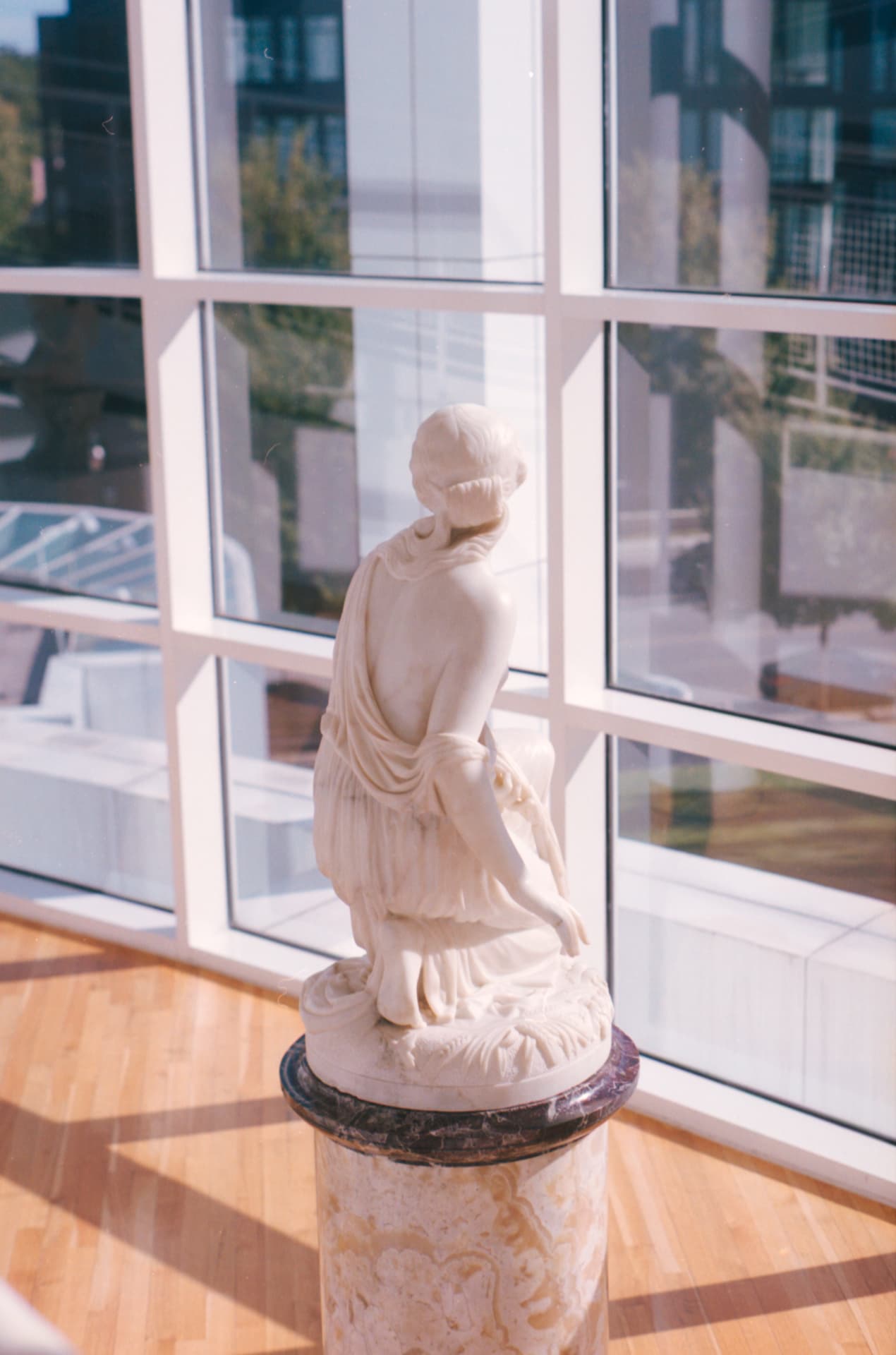 Marble sculpture on a plinth in front of a tall gridded gallery window