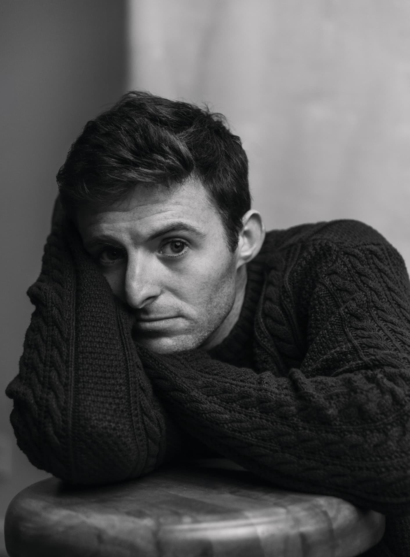 Black and white portrait of a man resting his head on his arms in a cable knit sweater