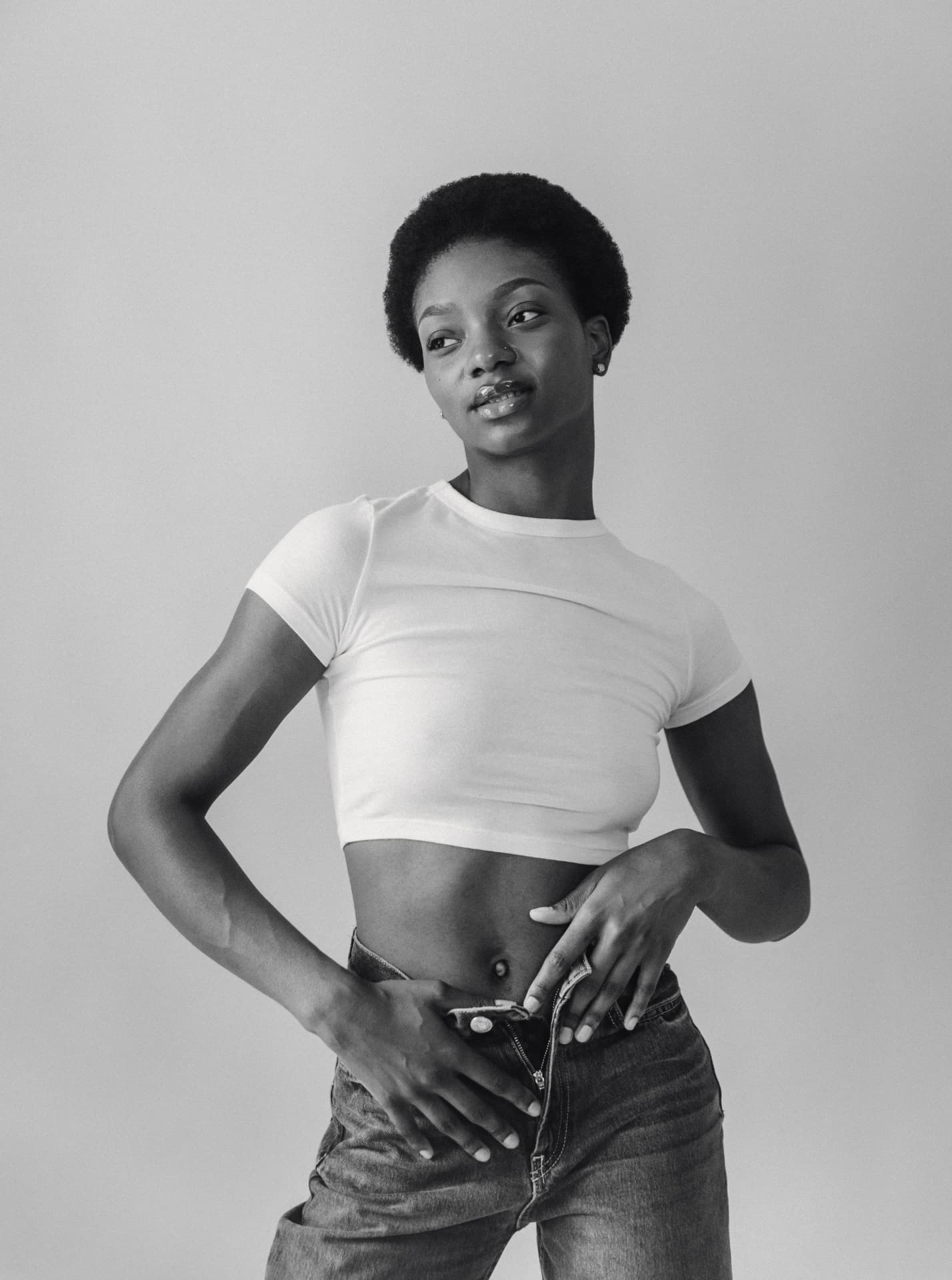 Black and white studio portrait in a white tee and denim against a grey backdrop
