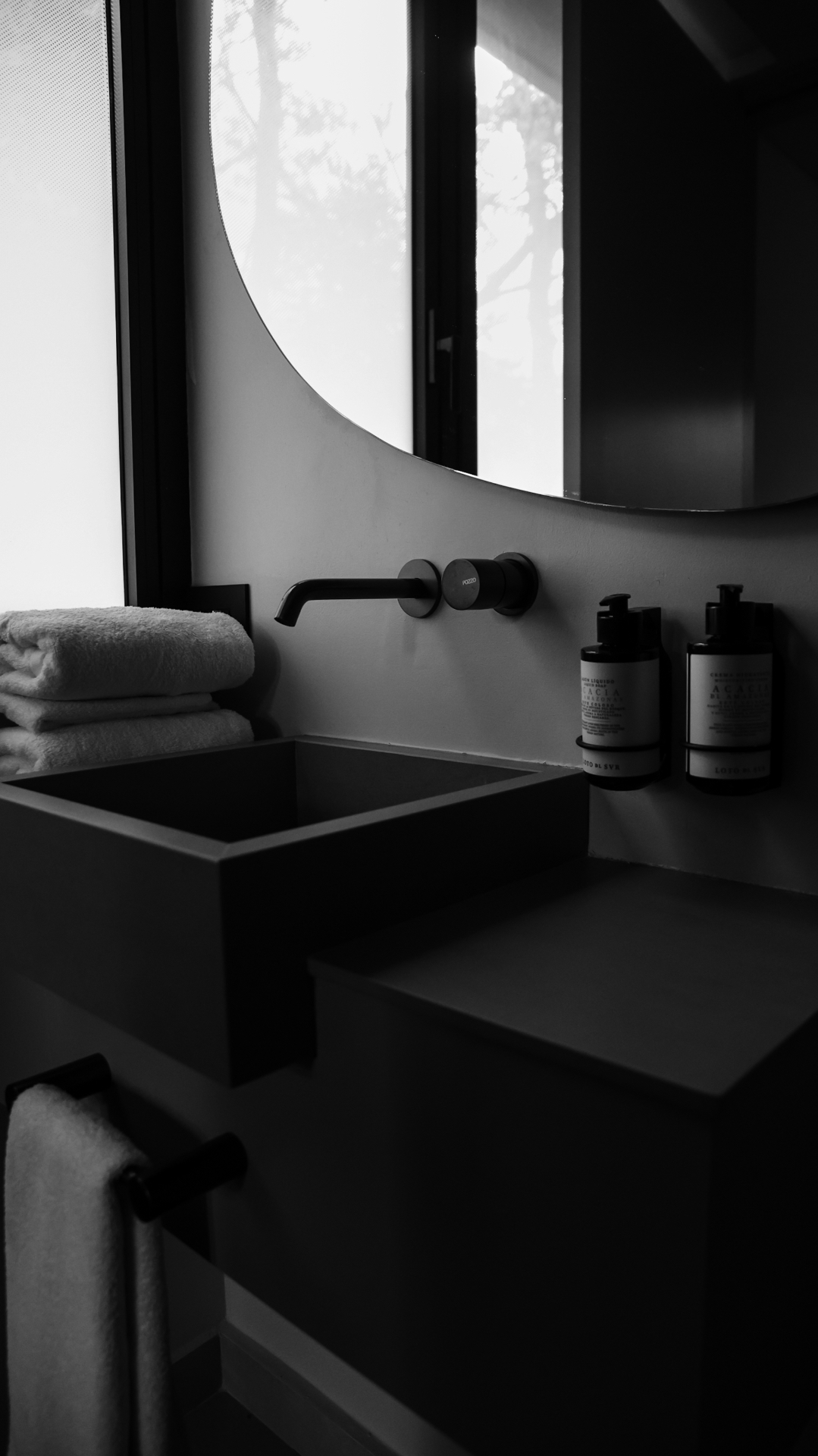 Black and white frame of a dark concrete basin and round mirror