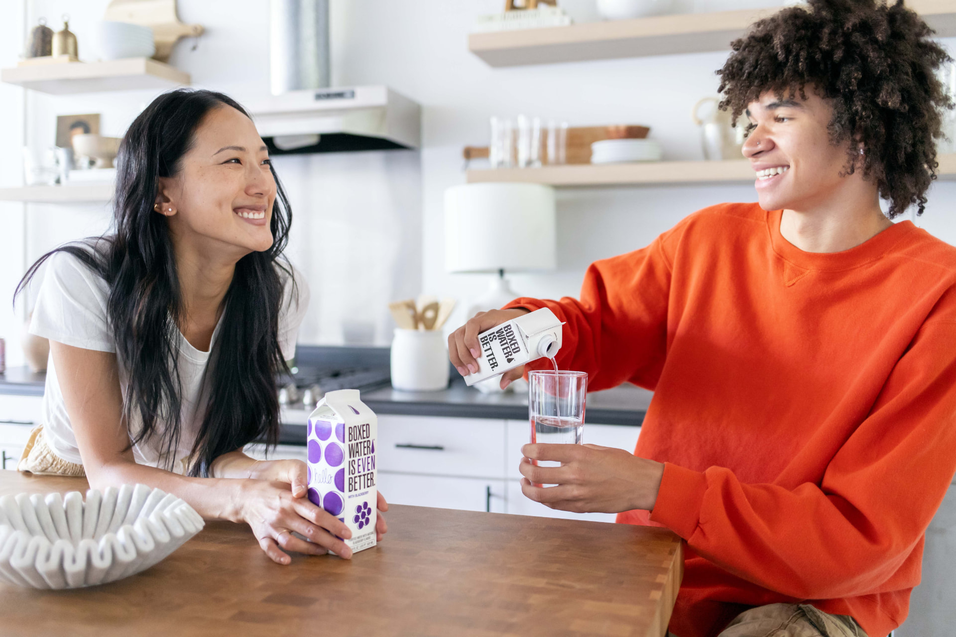 Two people in a kitchen pouring Boxed Water into a glass