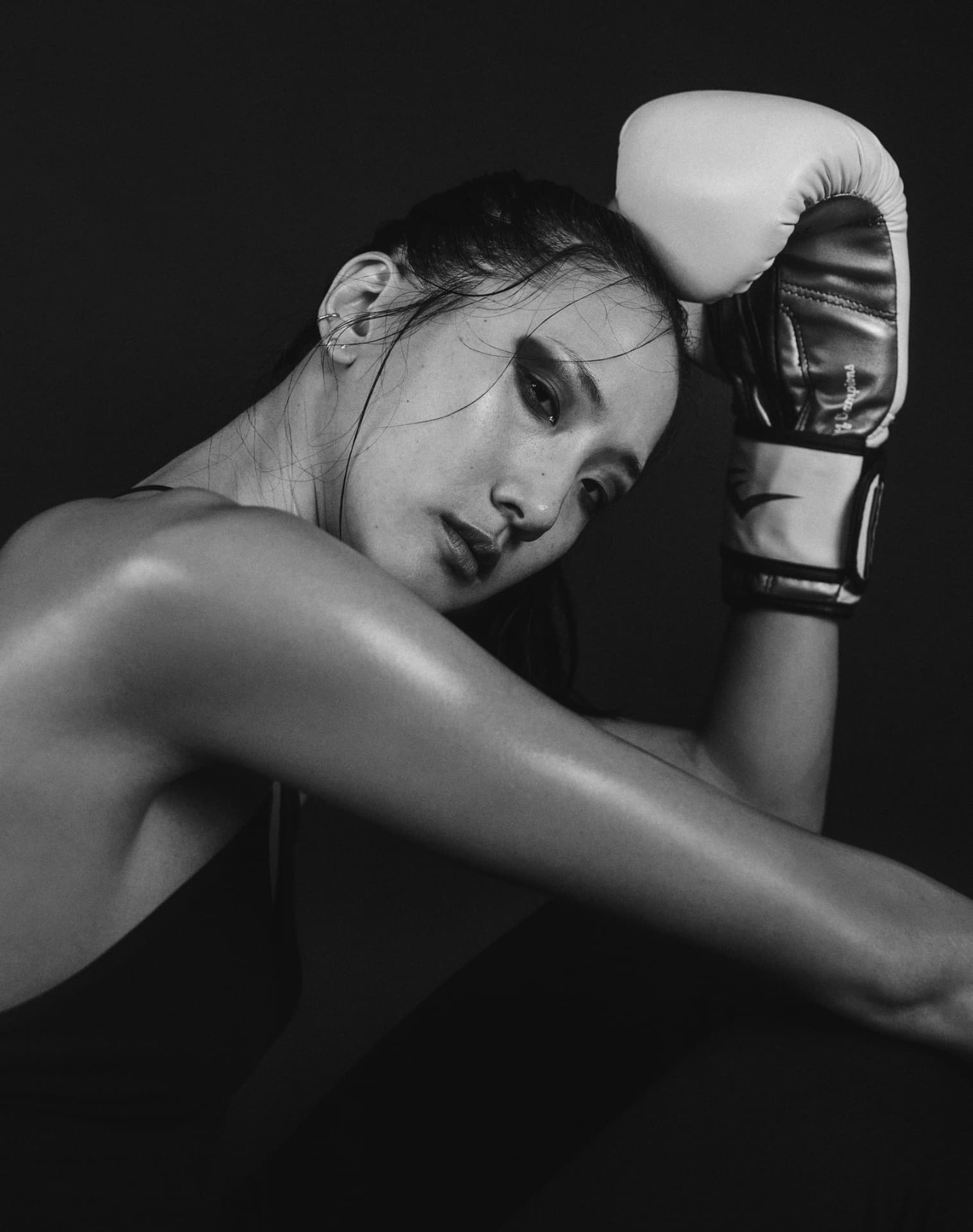 Black and white studio portrait of a boxer resting her head against a glove