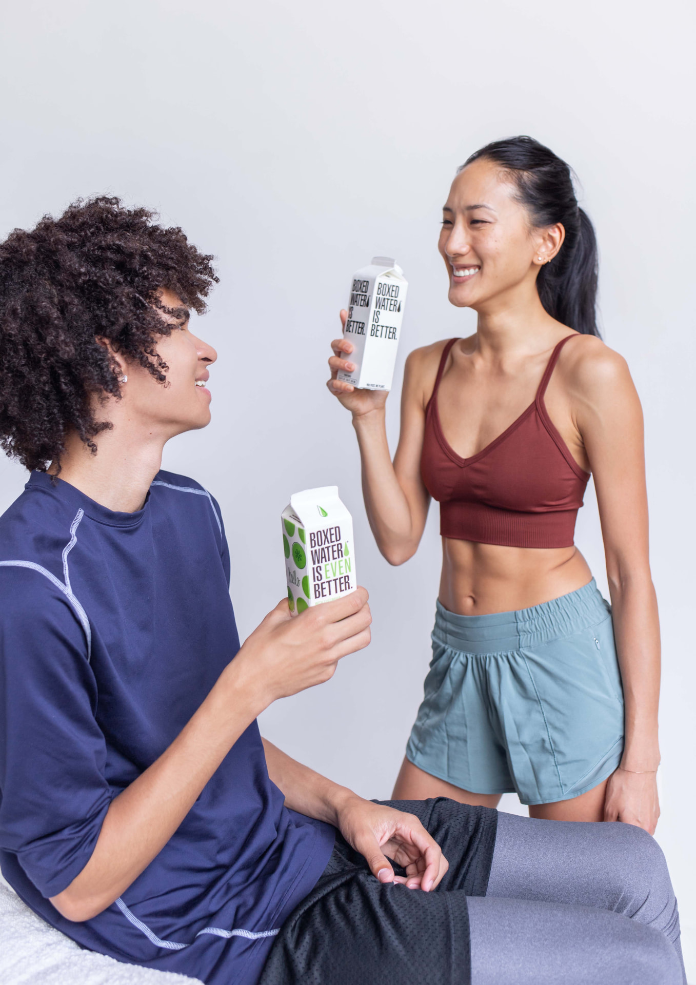 Two people in activewear holding Boxed Water cartons against a plain wall