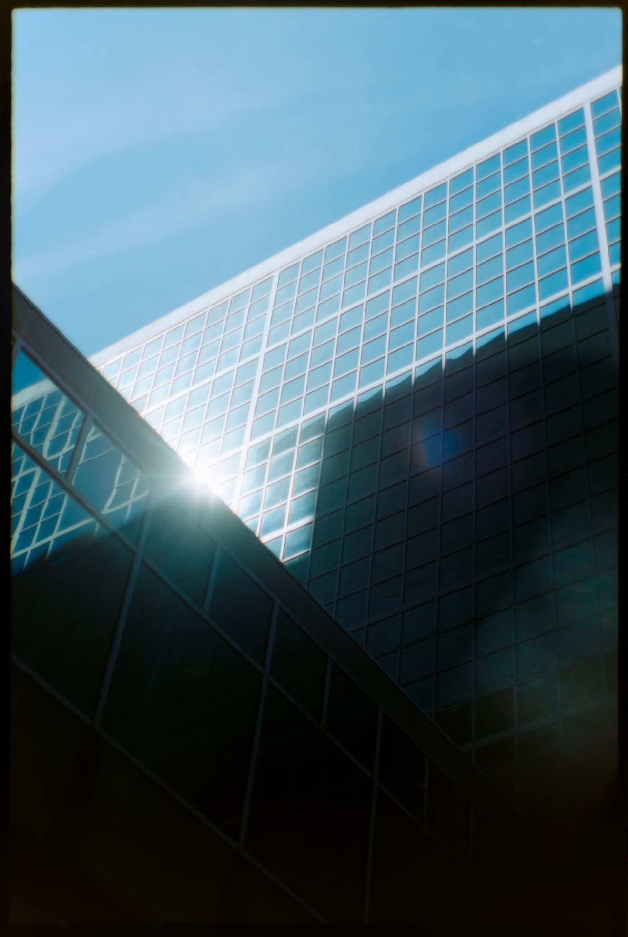 Sun flaring off the glass grid facade of a modern building against blue sky