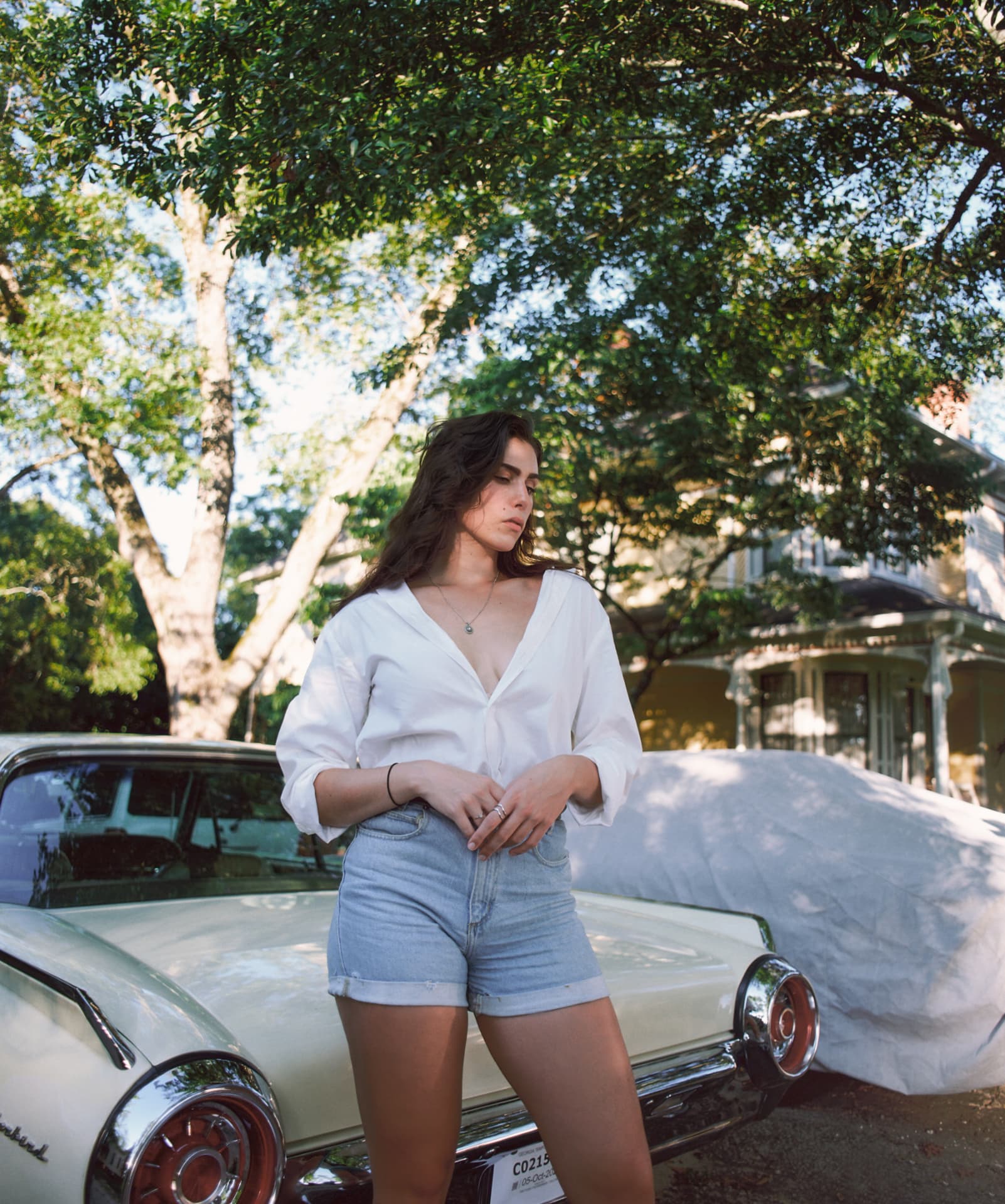 Portrait in a white shirt and denim shorts leaning on a vintage Thunderbird