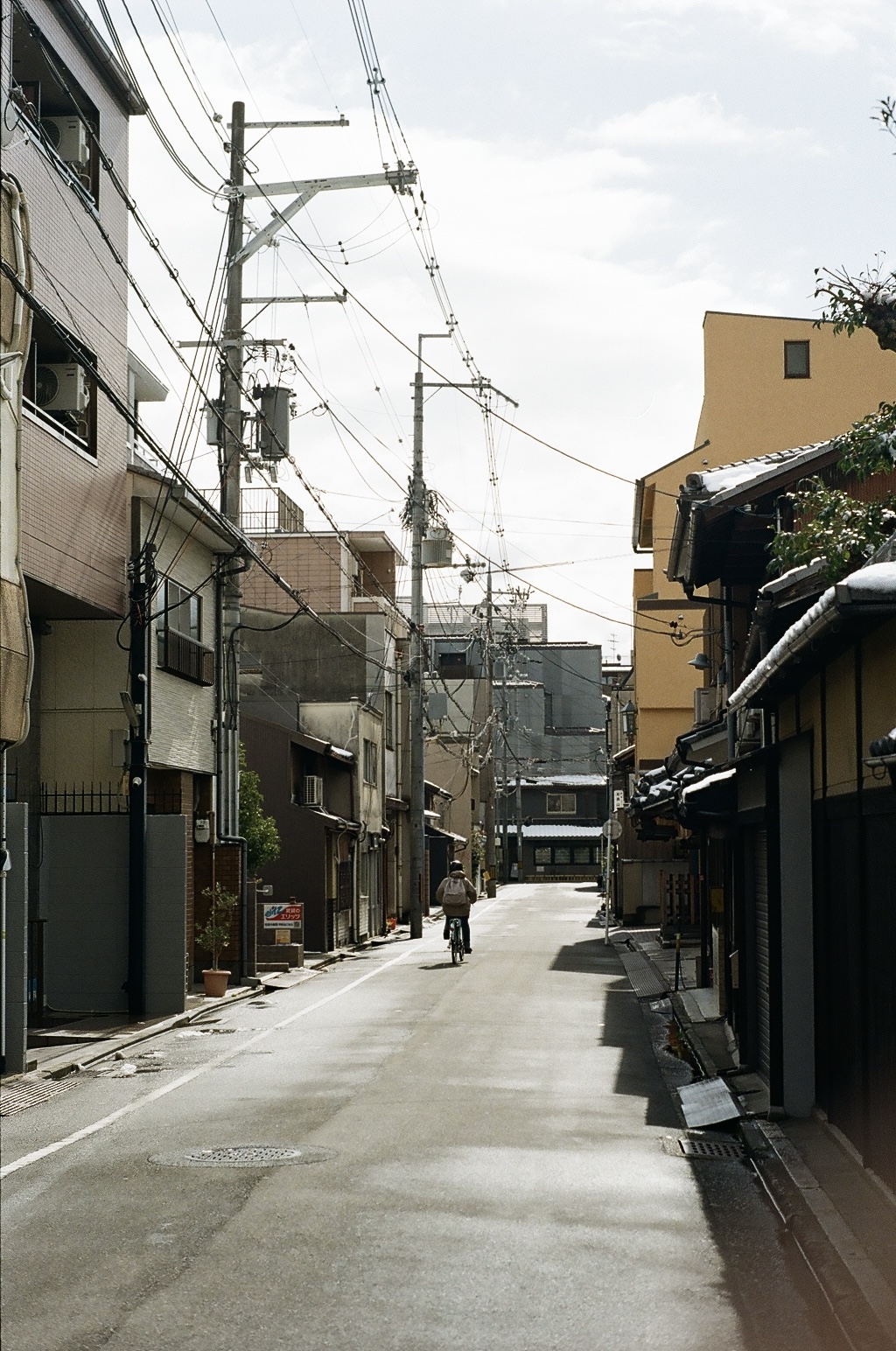 A cyclist far down a quiet street framed by tangled power lines
