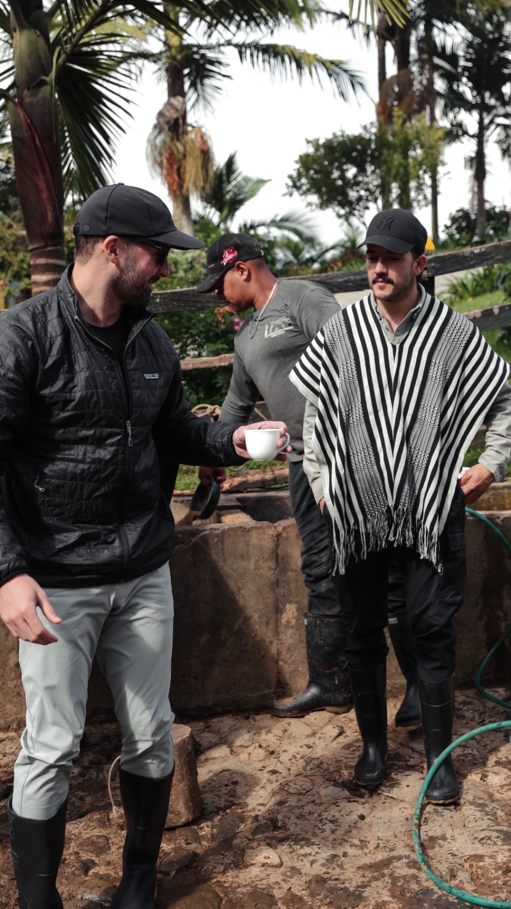 Men in boots on a farm, one handing over a cup of coffee