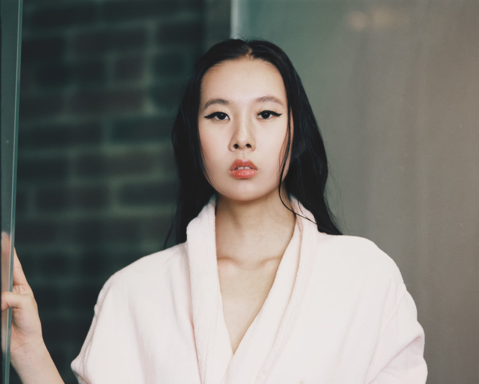 Beauty film portrait in a pale pink robe beside a glass door