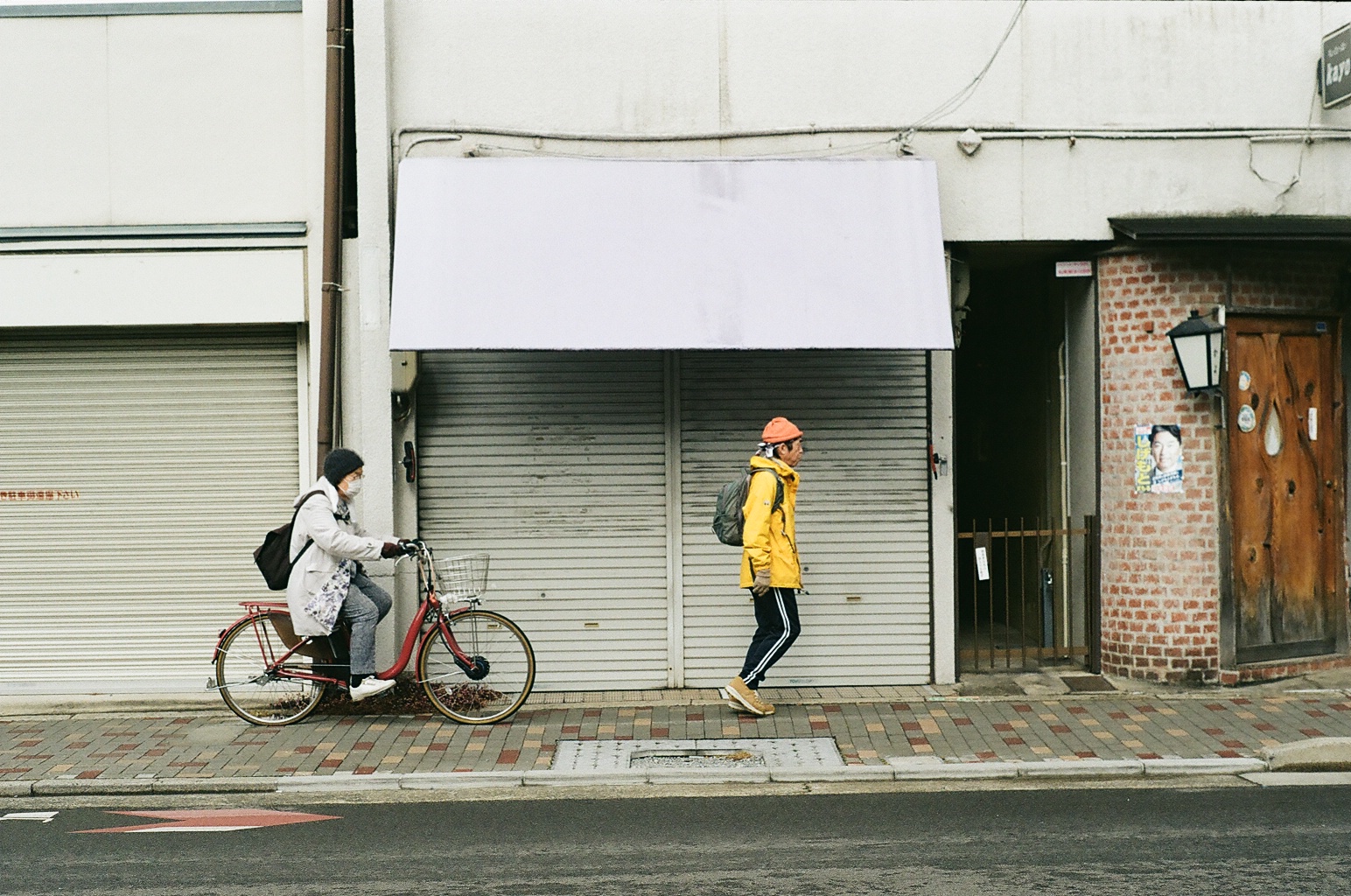 A cyclist and a man in a yellow jacket passing shuttered storefronts
