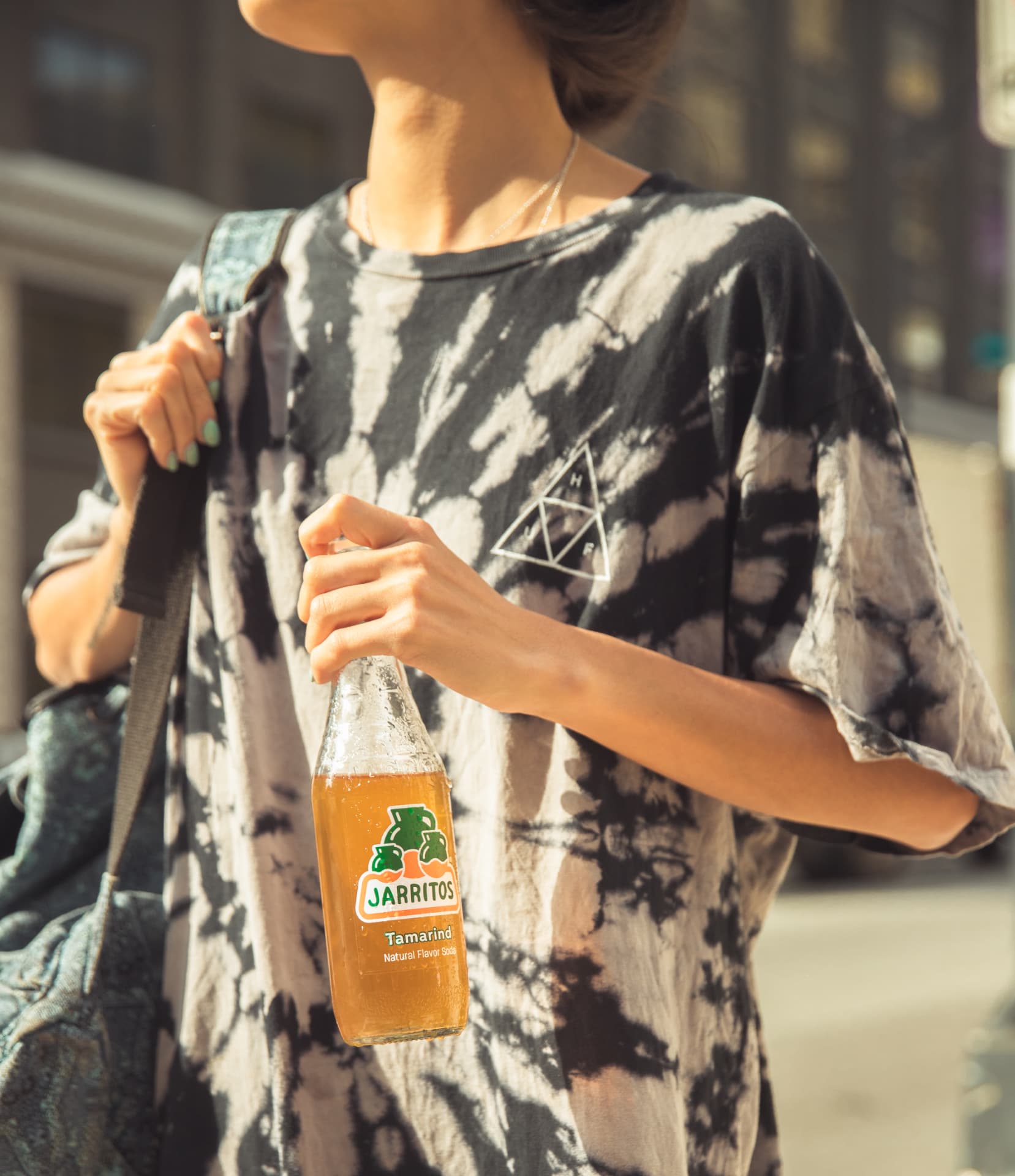 Cropped frame of a person in a tie dye tee carrying a tamarind Jarritos