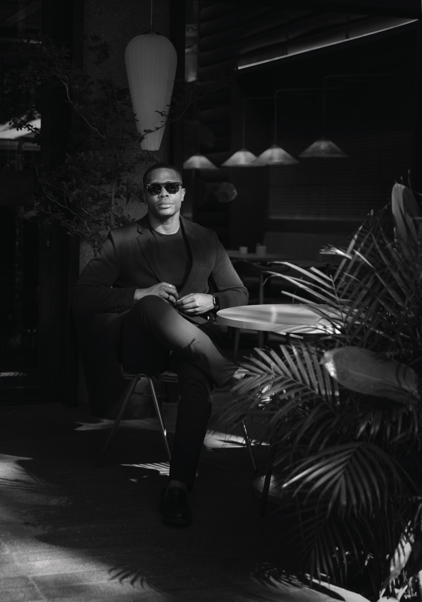 Black and white portrait of Lawrson Pinson seated at a cafe table in sunglasses