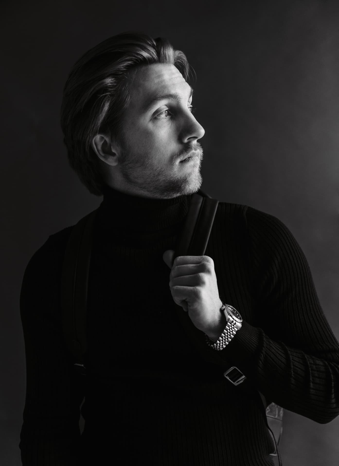Black and white studio portrait of a man in a black turtleneck with a bag strap