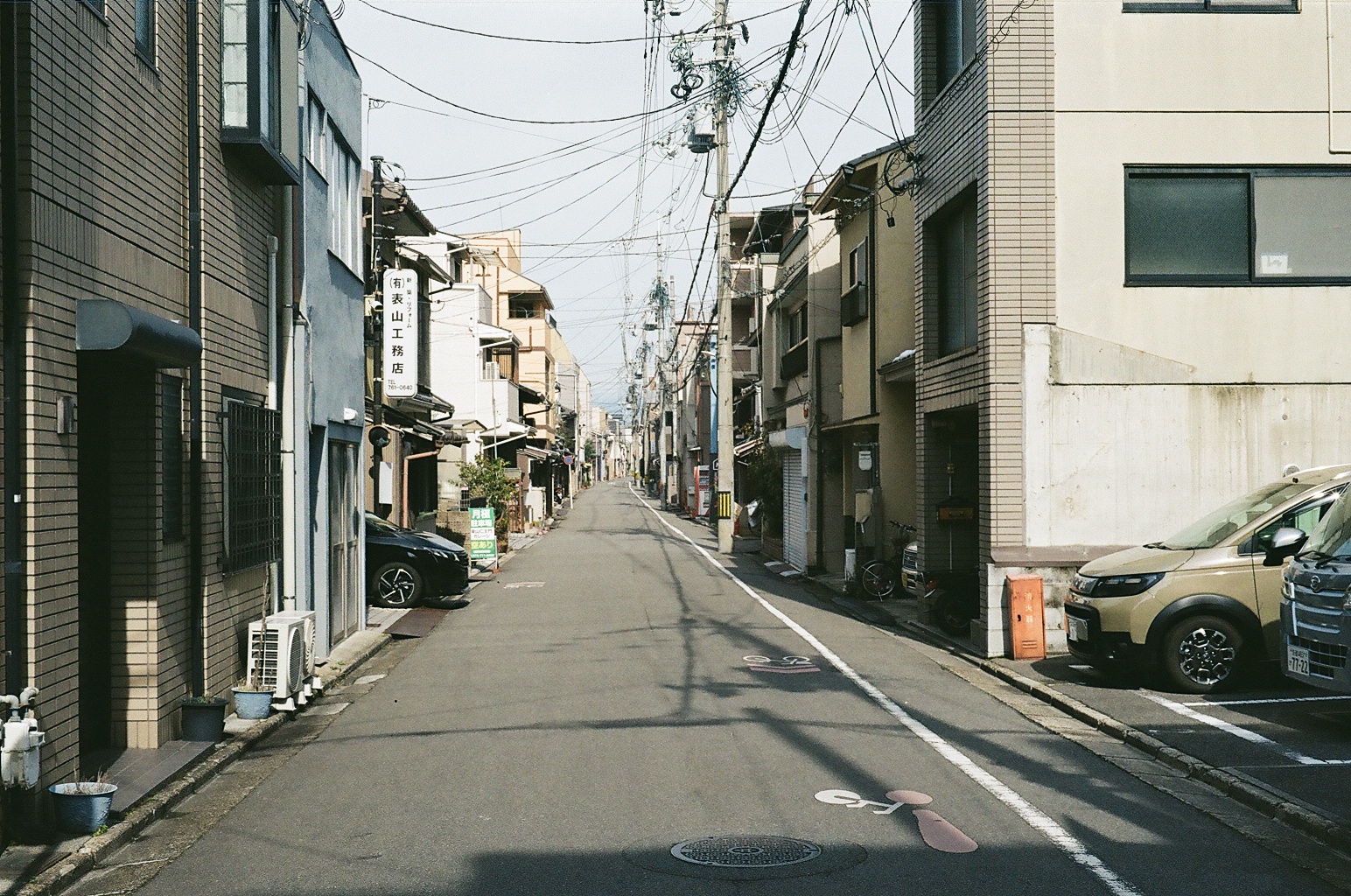 Empty residential street lined with parked cars and power lines