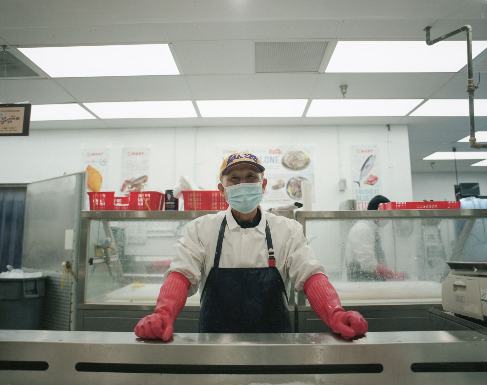 Documentary portrait of a fishmonger in pink gloves behind a market counter