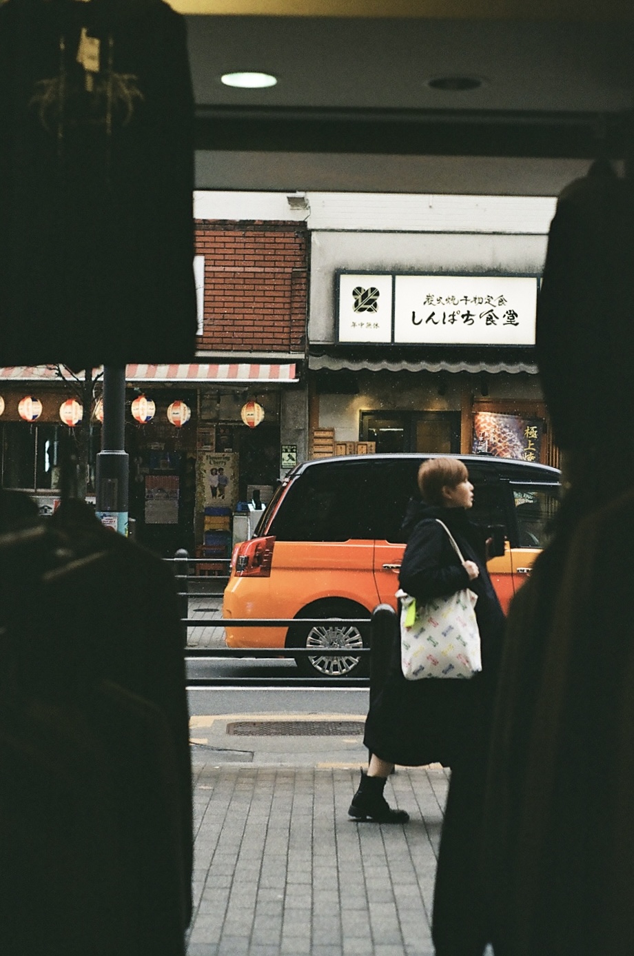 A person walking past an orange van and a lit restaurant sign